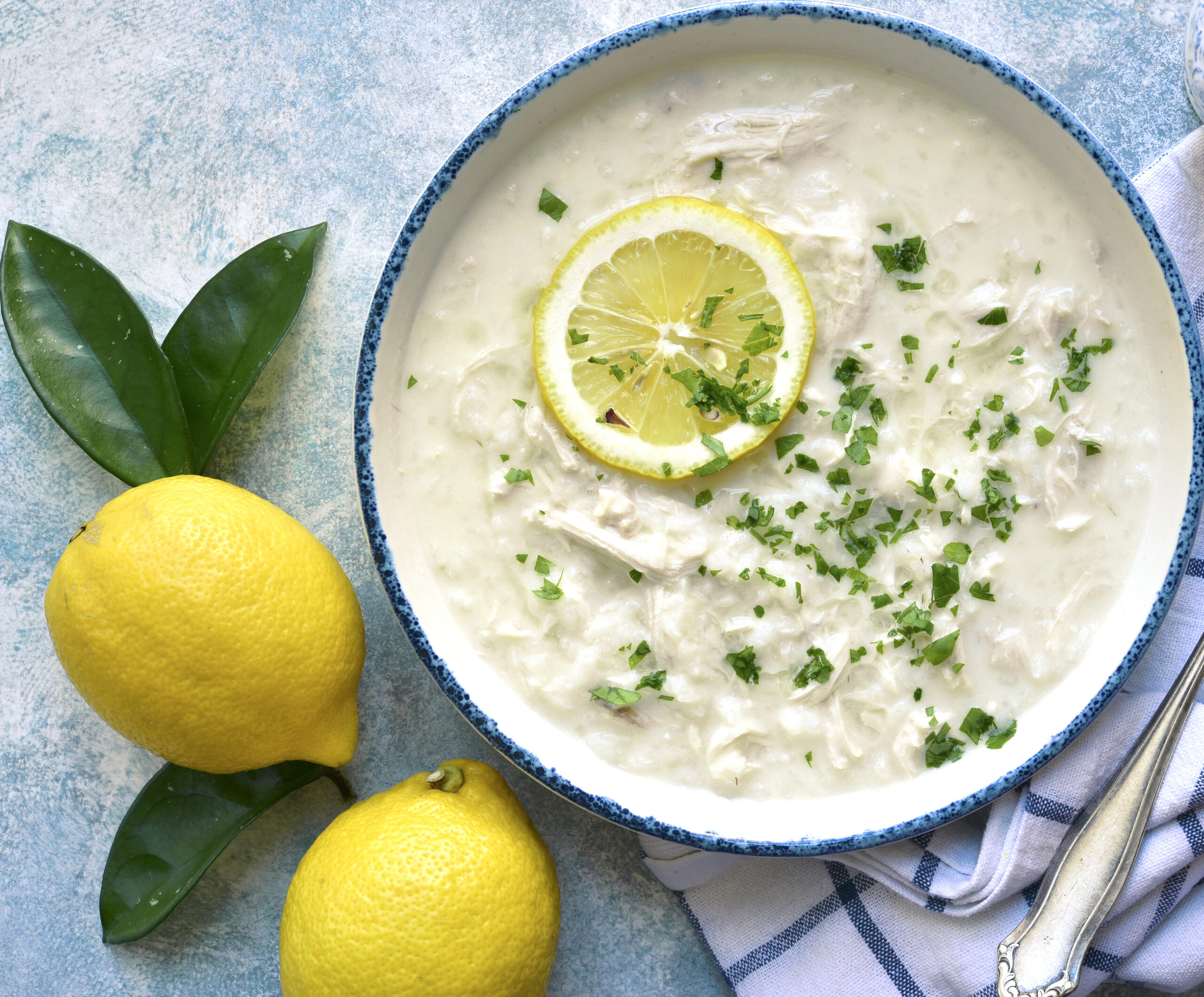 Overhead of bowl of soup on blue background with lemons