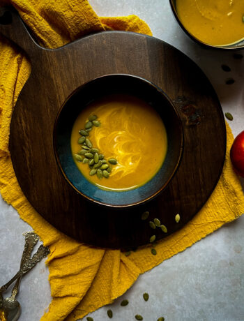 Overhead of butternut squash soup in a blue bowl on a brown board with a mustard colored napkin underneath