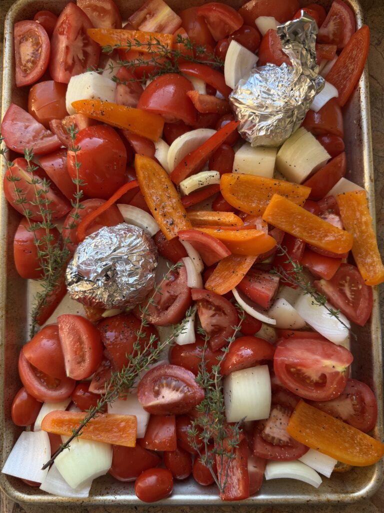 overhead shot of diced tomatoes, bell peppers, onions and garlic wrapped in foil on a sheet pan