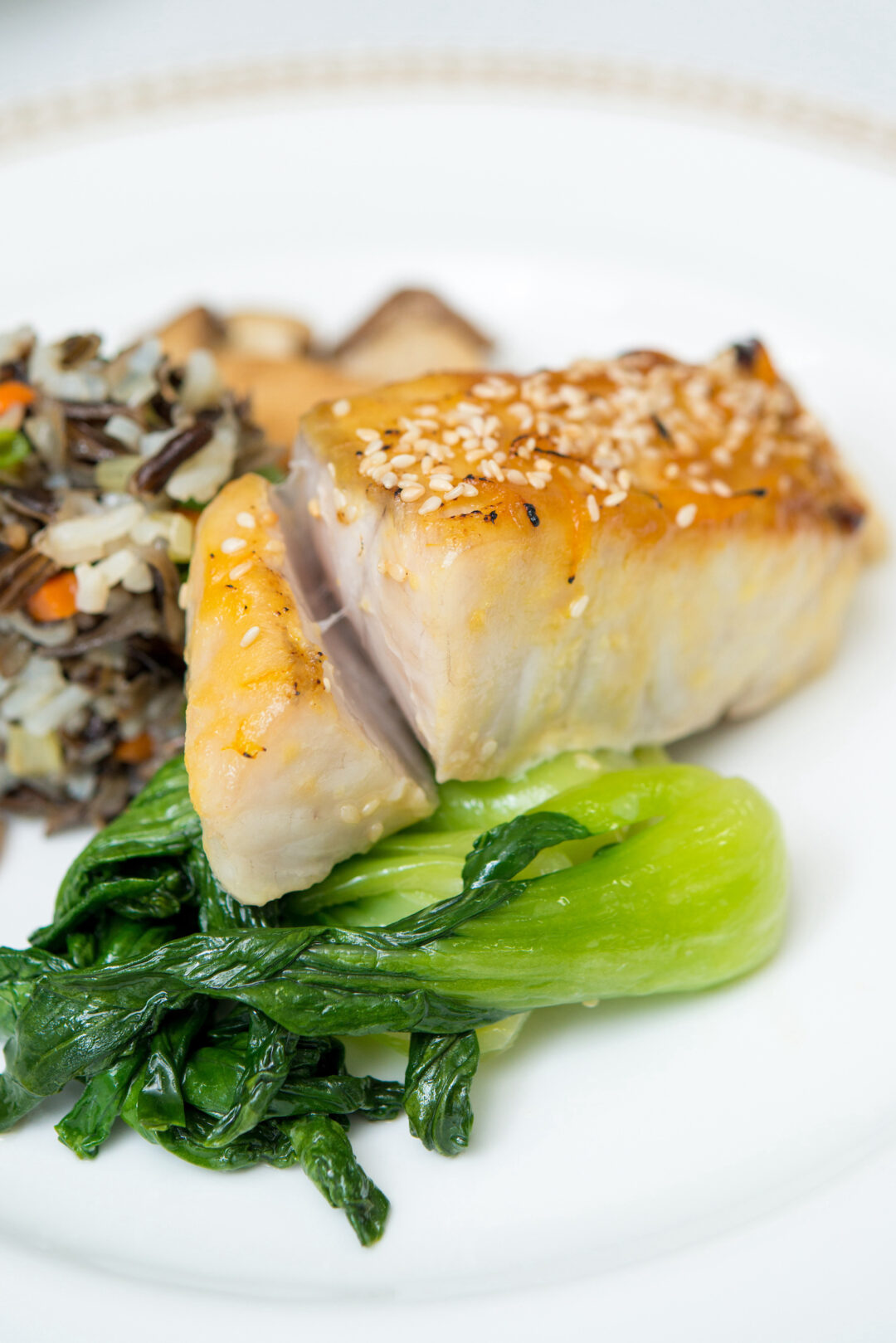 Close up of miso glazed sea bass on white plate with bok choy and wild rice