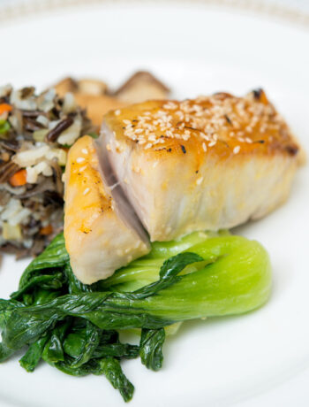 Close up of miso glazed sea bass on white plate with bok choy and wild rice