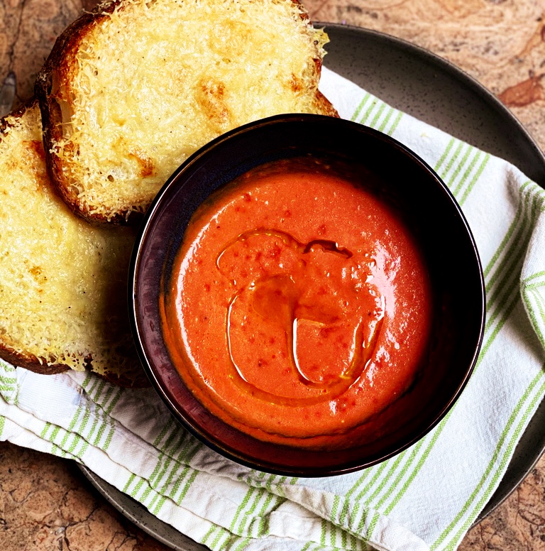 overhead photo of tomato soup in a dark bowl with cheese toast