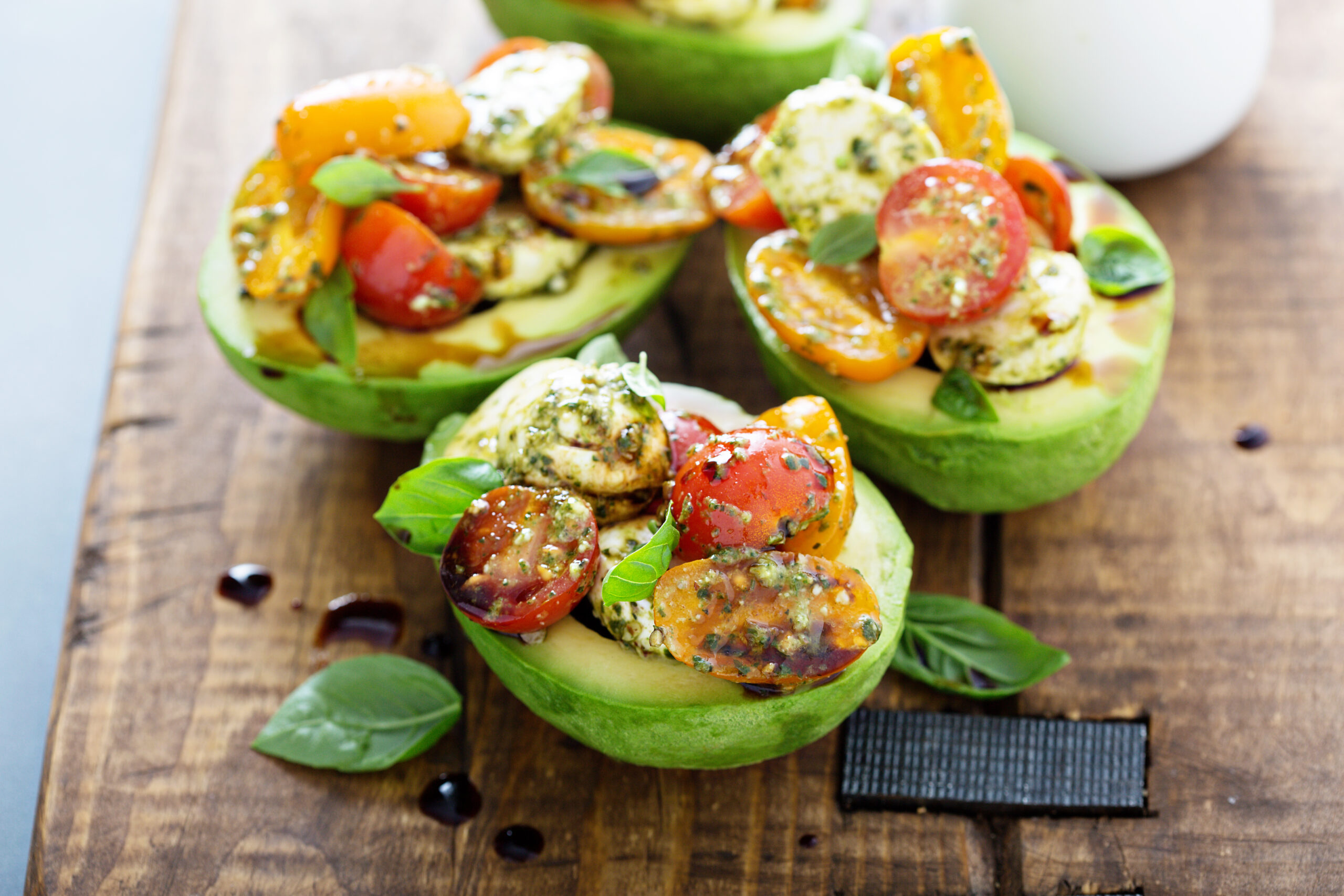 Overhead of avocados stuffed with tomatoes, mozzarella and basil on wood board