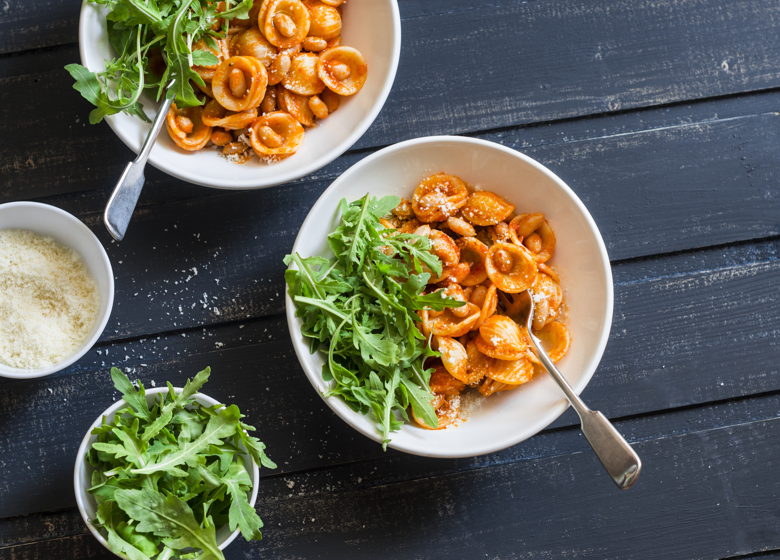 overhead of orecchiette pasta tossed in a shallot and cherry tomato sauce with a side arugula salad