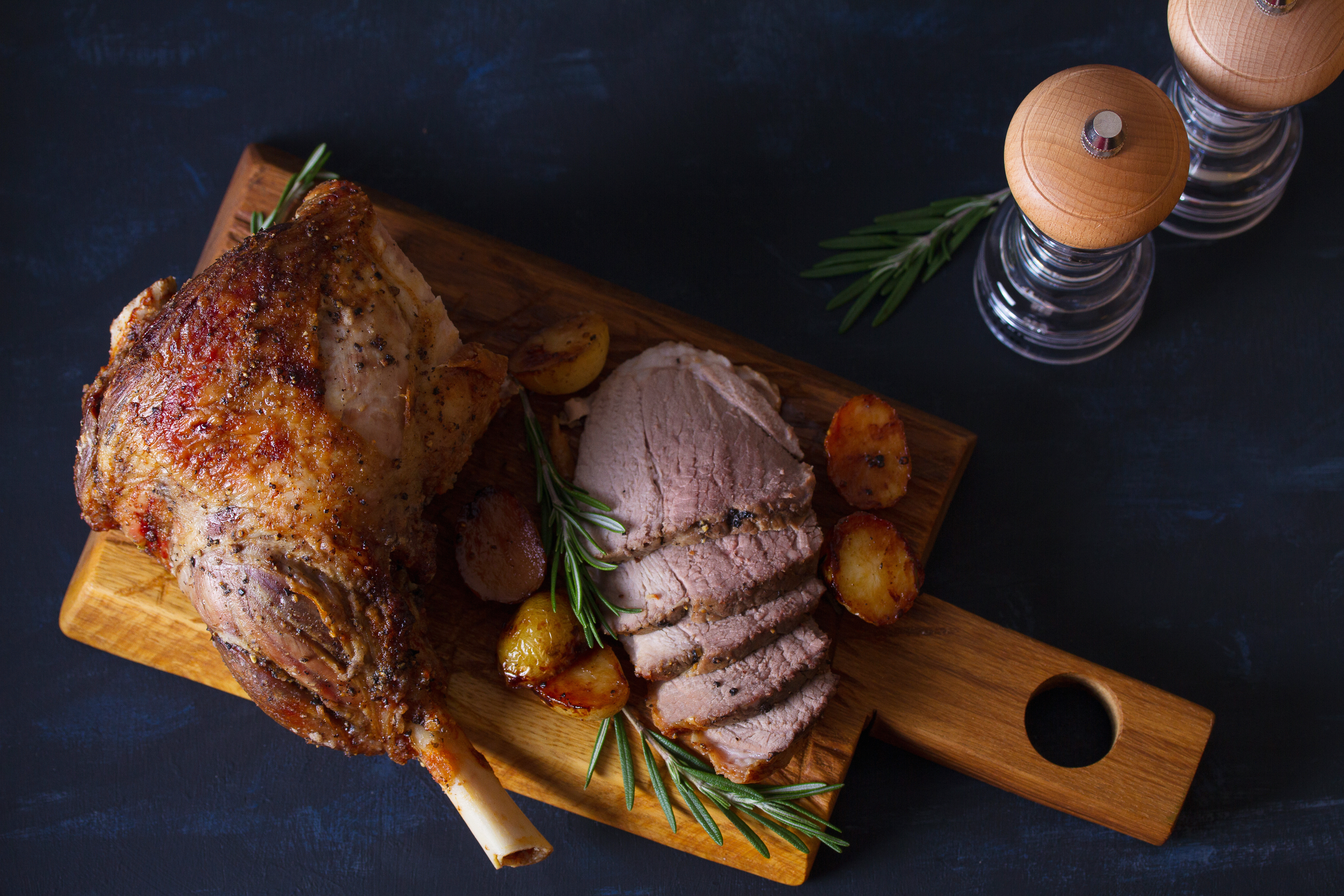 Roast leg of lamb with potatoes and rosemary on serving wooden board