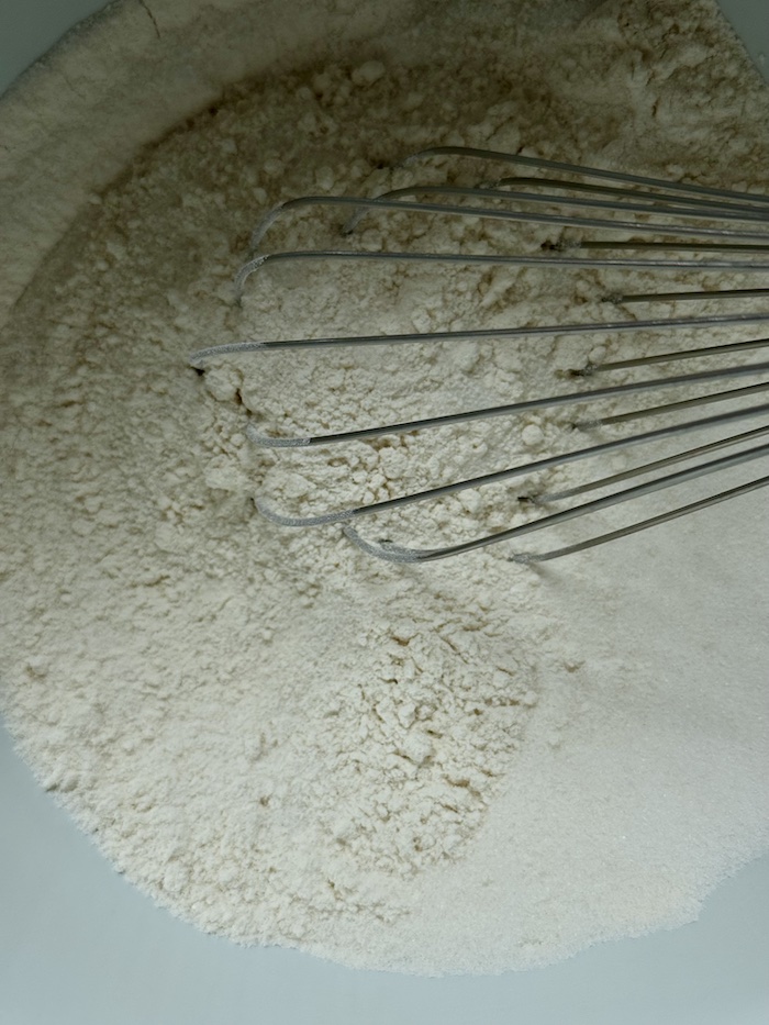 overhead of flour for blackberry dump cake batter in mixing bowl with whisk