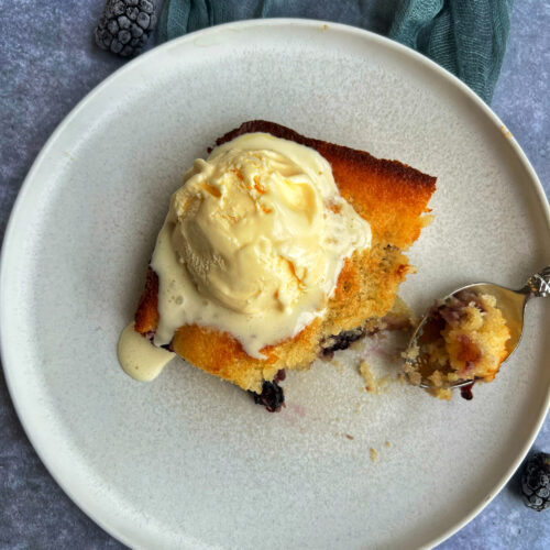 Overhead photo of blackberry dump cake on white plate topped with vanilla ice cream