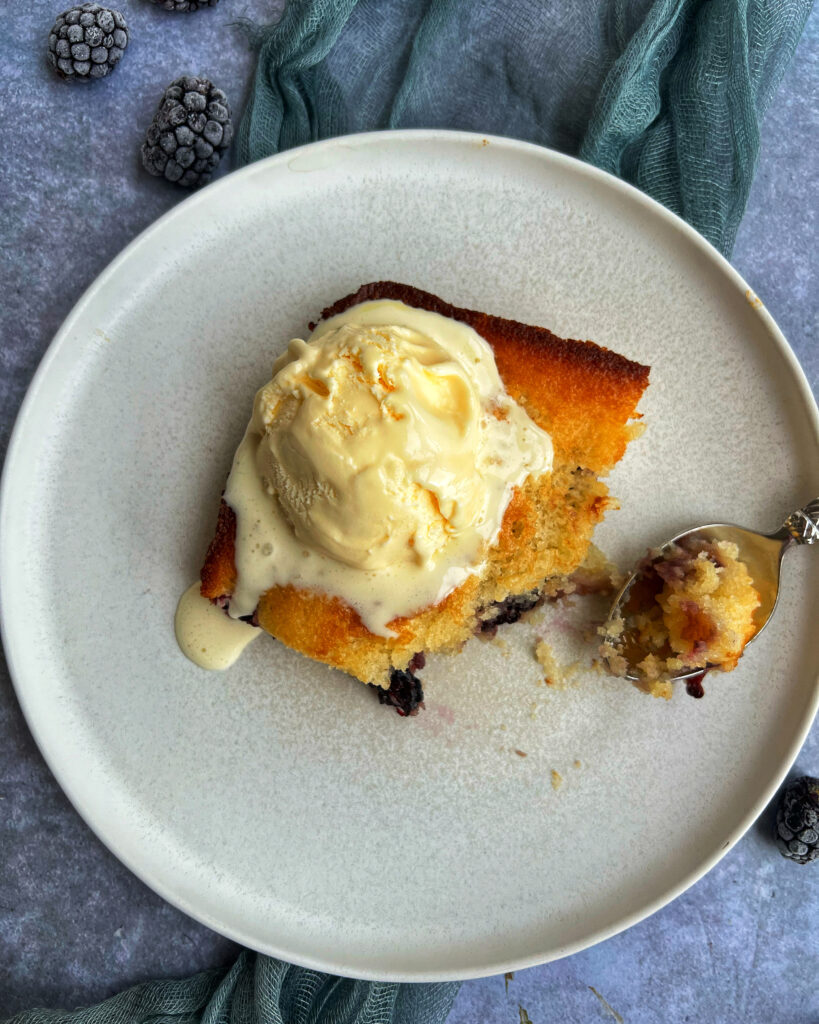 Overhead photo of blackberry dump cake on white plate topped with vanilla ice cream
