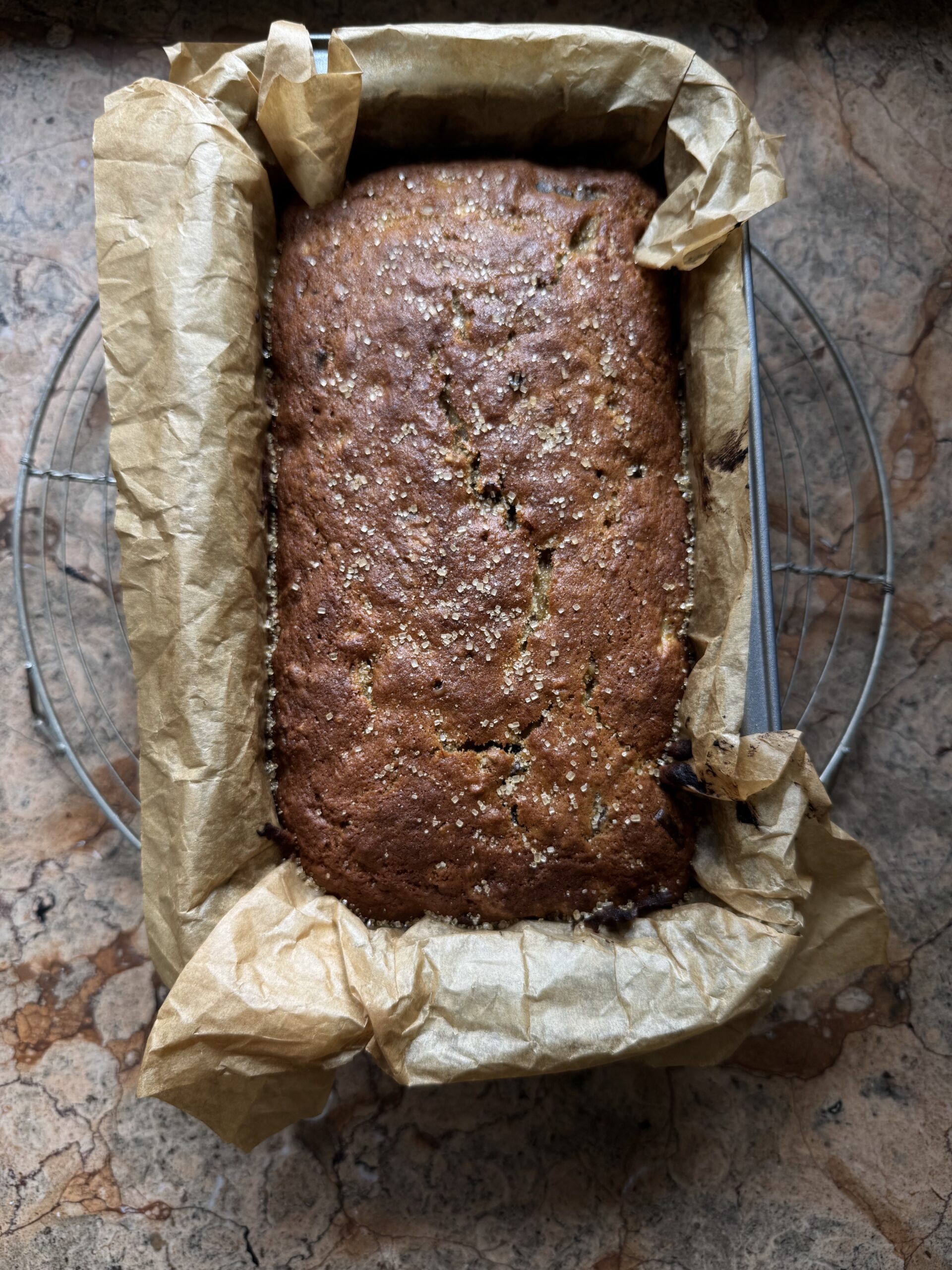 Overhead photo of baked Chocolate Chunk Banana Bread in parchment lined loaf pan on wire cooling rack