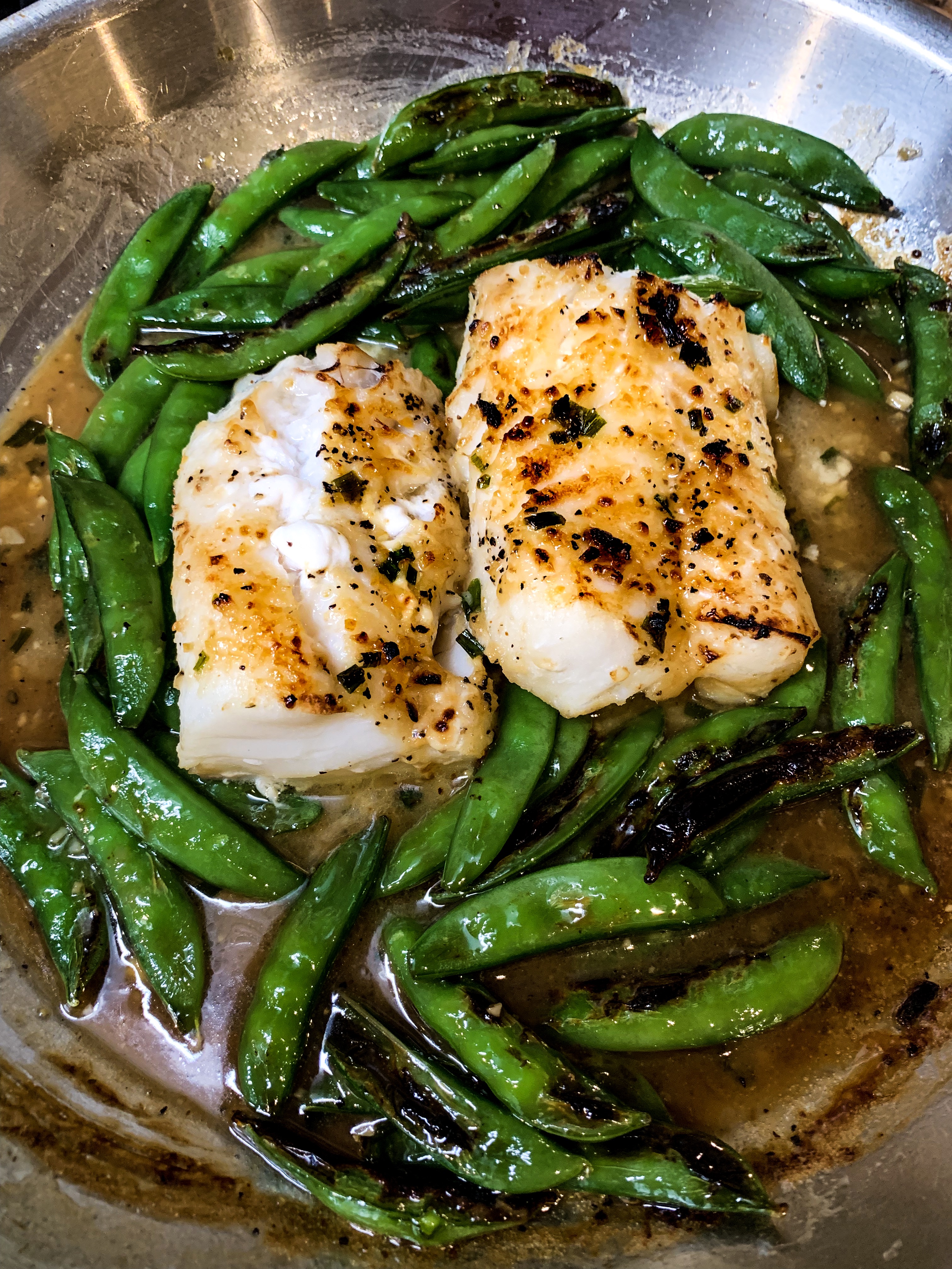 overhead of broiled miso-butter cod with snap peas in a skillet