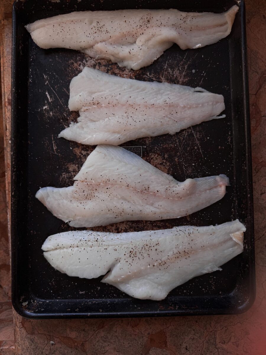 overhead photo of uncooked cod on rimmed baking sheet