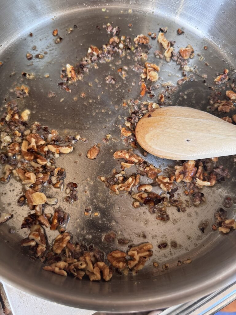 toasted walnuts in skillet with wooden spoon.