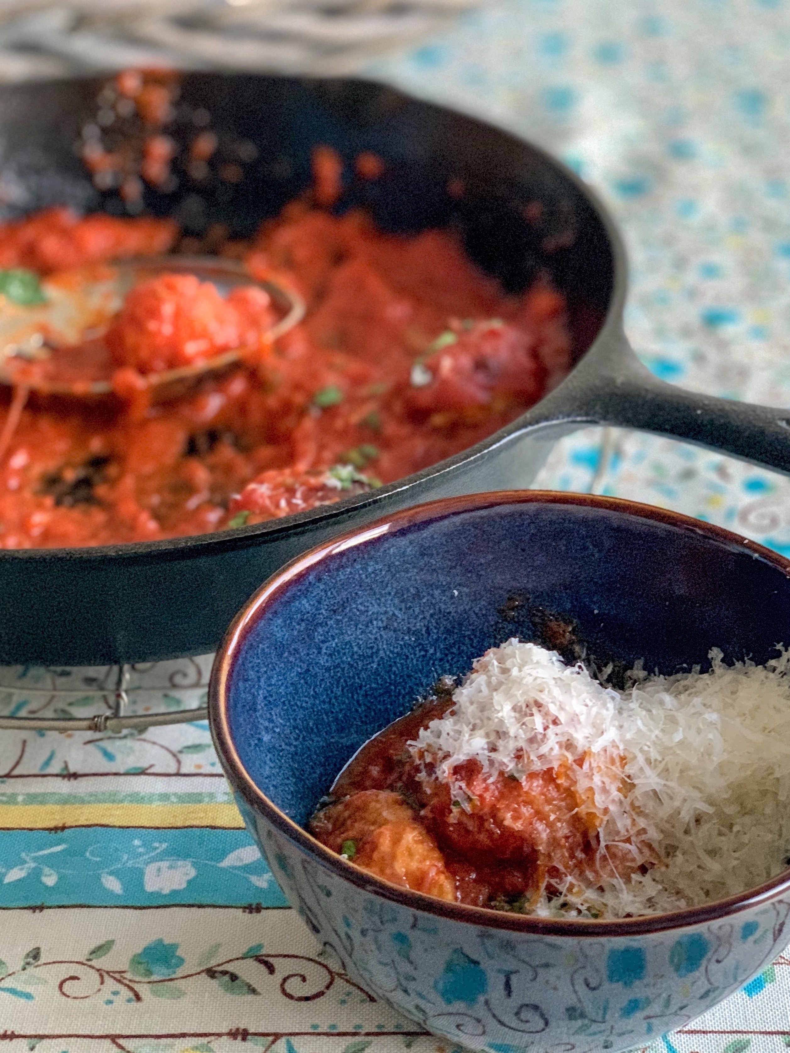 overhead photo of meatballs in a bowl with a skillet behind filled with more meatballs in marinara sauce