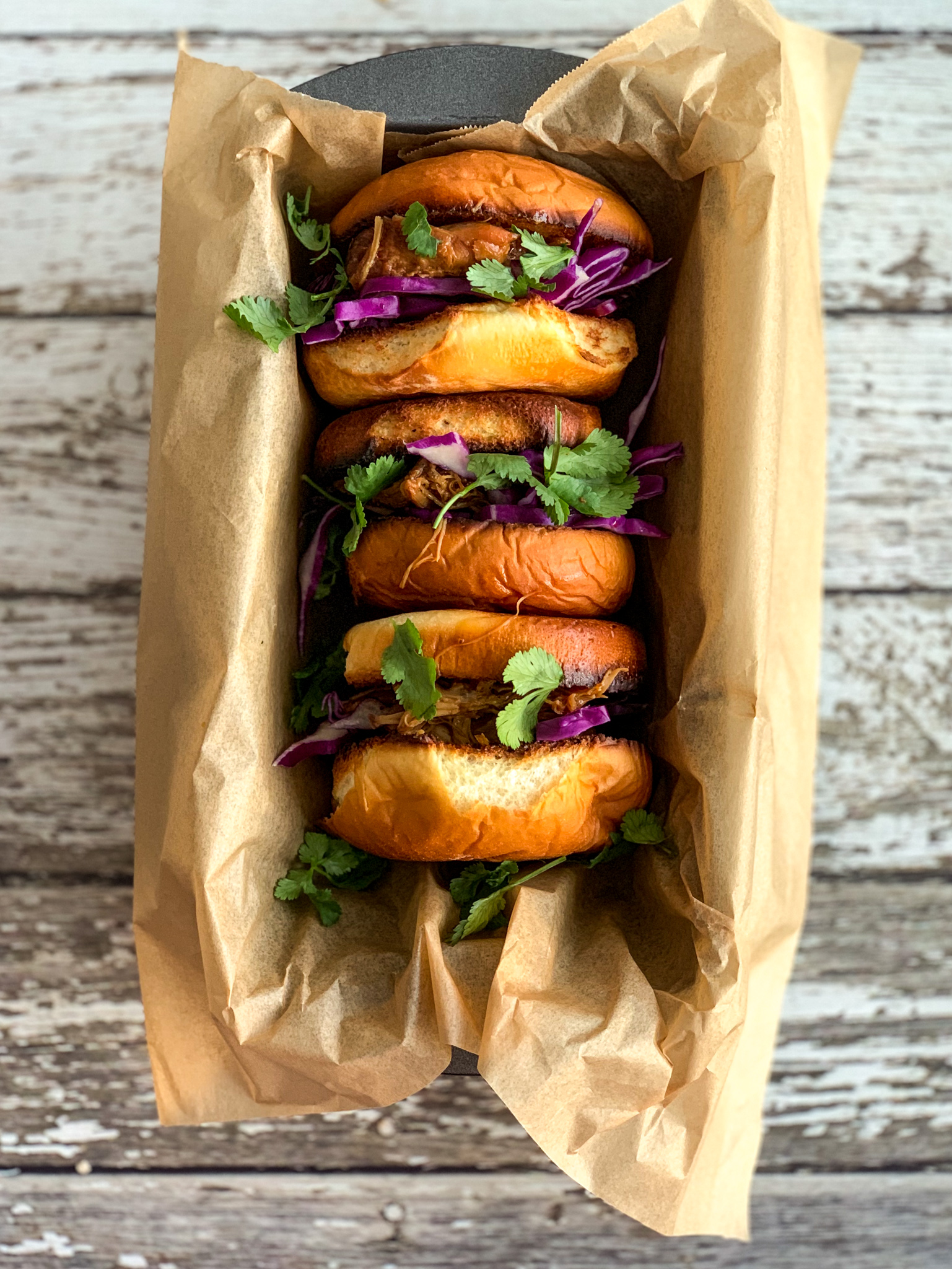 Overhead photo of 3 pulled pork sandwiches on parchment with wood board background