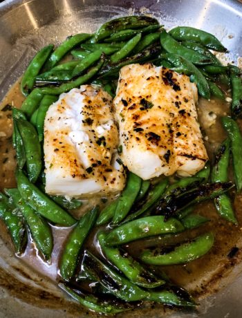 overhead of cod in a skillet surrounded with charred snap peas