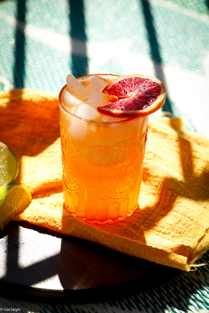 Angled view of citrus summer mule in a glass on mustard yellow cloth with blood orange slice