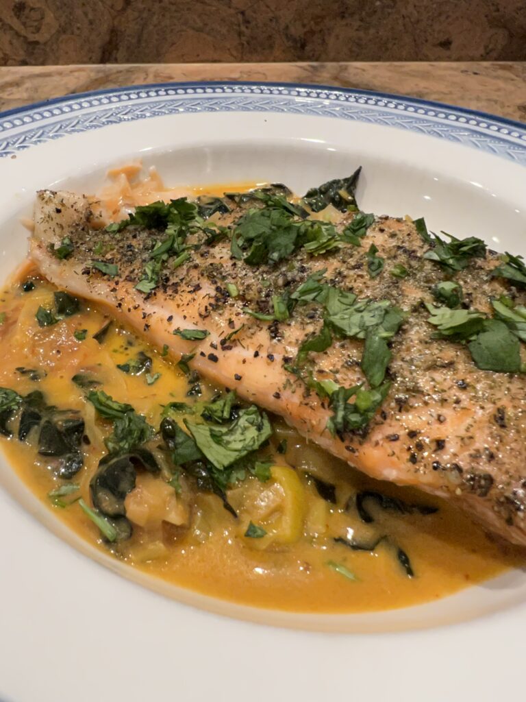 side view of salmon with kale and tomatoes on white plate with blue rim