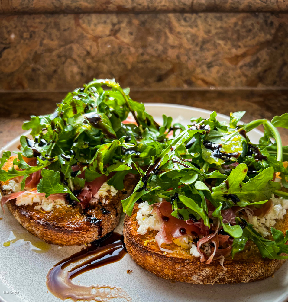 Side view of open face sandwich with slices of prosciutto and arugula on a plate