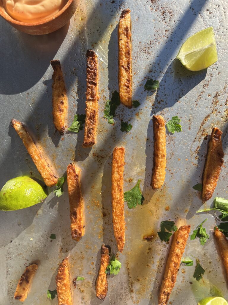 overhead of jicama fries on sheet pan with lime wedges, parsley and sauce