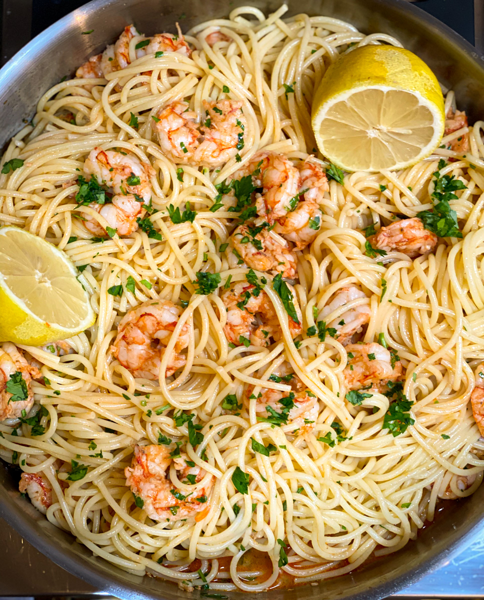 Overhead shot of spaghetti and shrimp in skillet with halved lemon