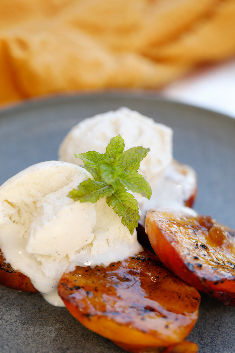 Overhead of grilled peaches on a grey plate with vanilla ice cream and sprig of mint
