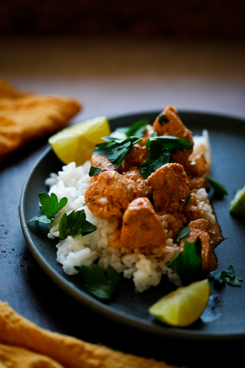 Overhead of chicken harissa over rice on a black dish.