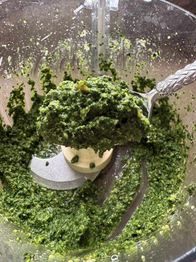 Close up photo of kale pesto on spoon over the food processor