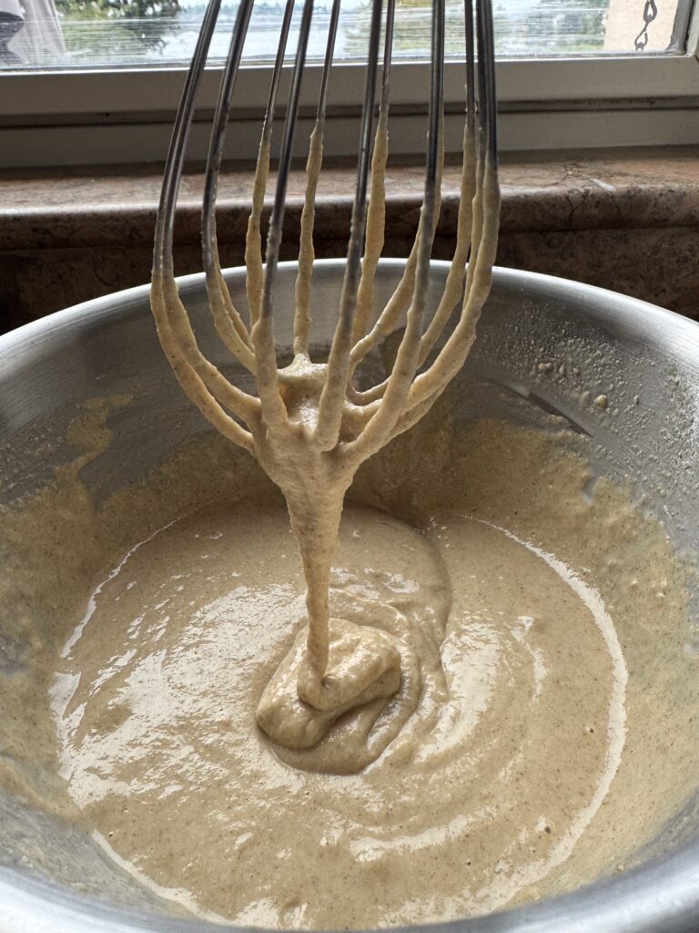 side photo of whisk with kodiak pancake batter dripping off the bottom back into stainless steel bowl
