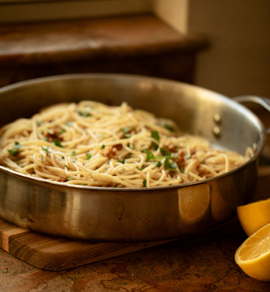 spaghetti in a stainless steel skillet with sliced lemon on counter
