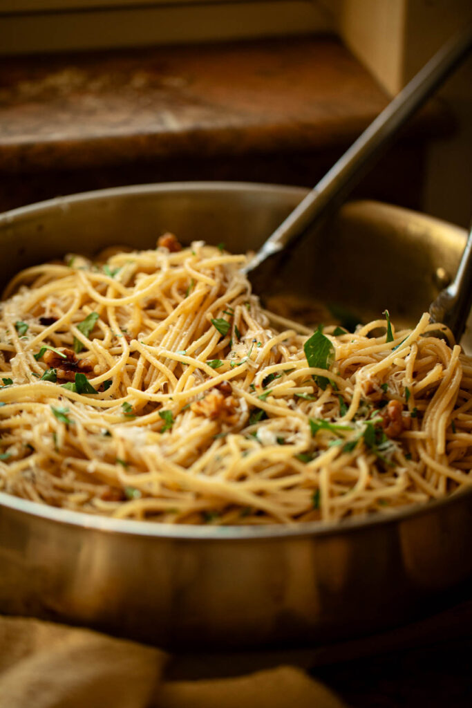 spaghetti in a stainless steel skillet with tongs