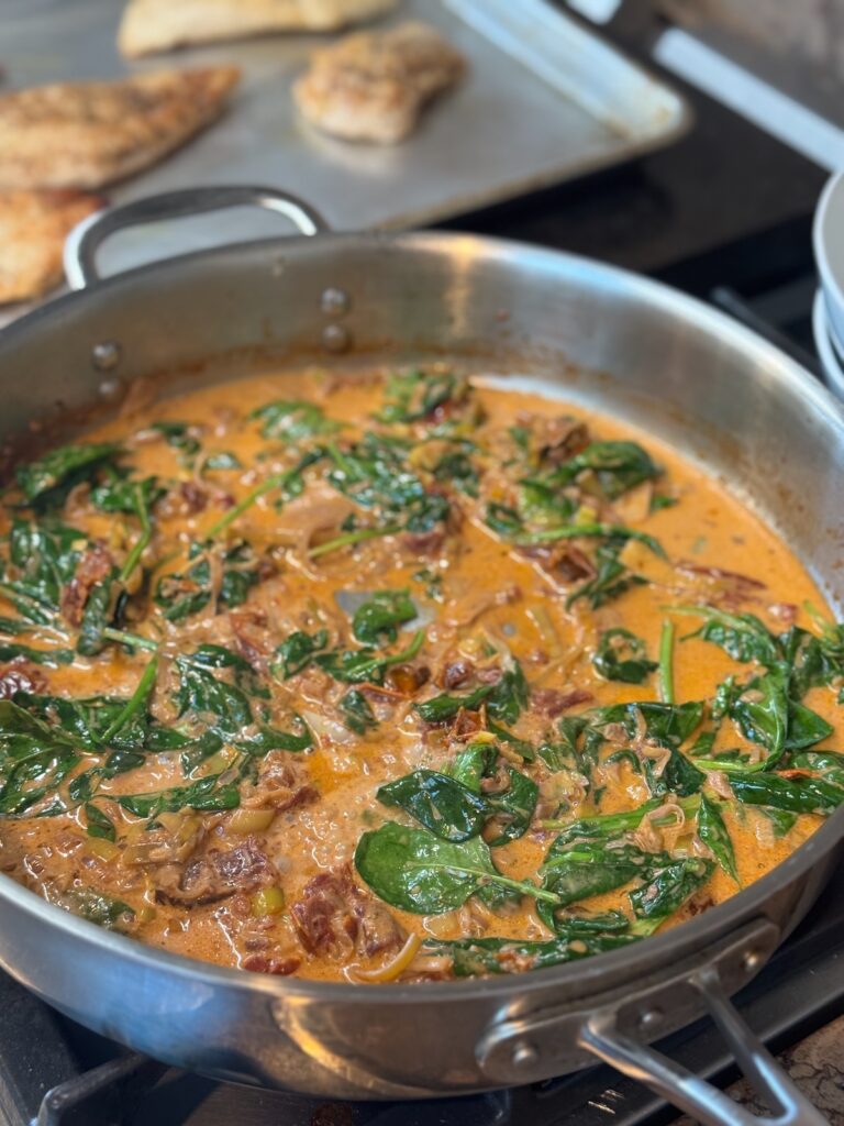 sundried tomato and spinach sauce in skillet with chicken on baking sheet
