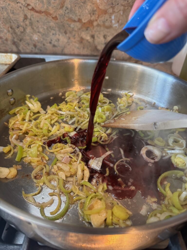 red wine being poured into a skillet with leeks and butter