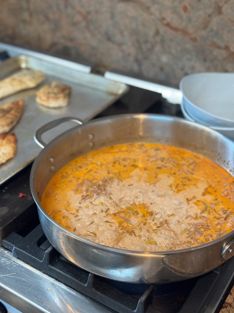 tomato sauce simmering in skillet on stove with baking sheet with chicken in the background