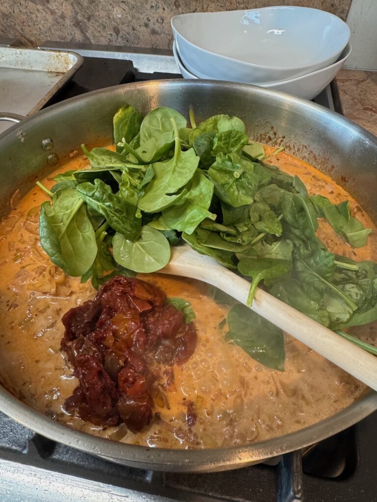 spinach and sundried tomatoes added to sauce in skillet